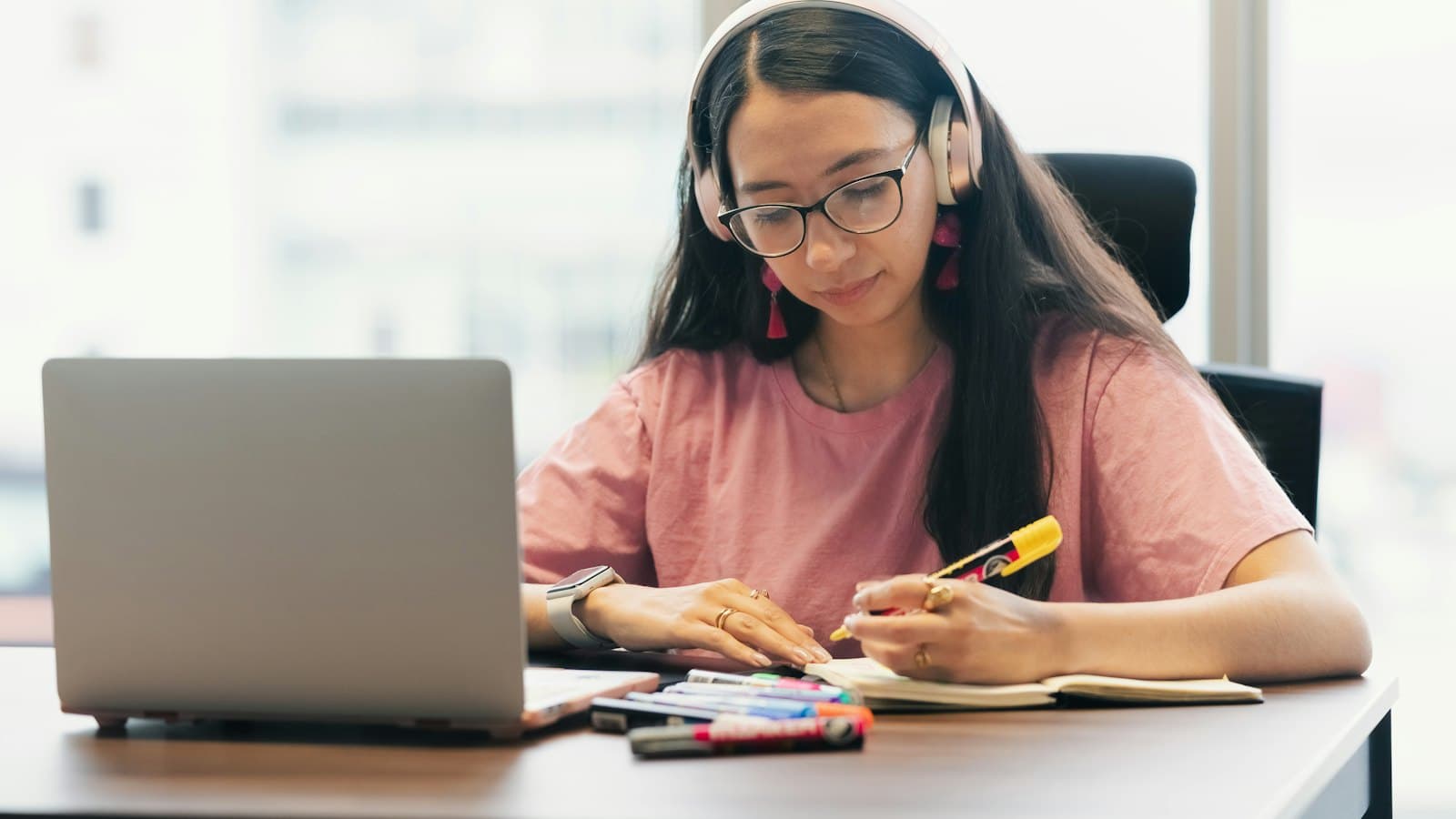 Young woman wearing headphones studying with notes at her desk