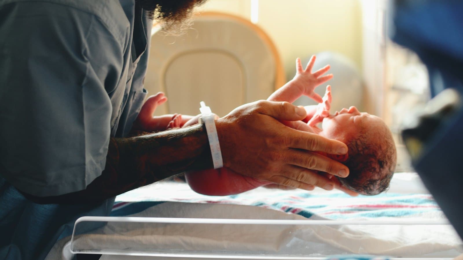 Newborn baby being gently lifted onto a hospital cot by caring hands