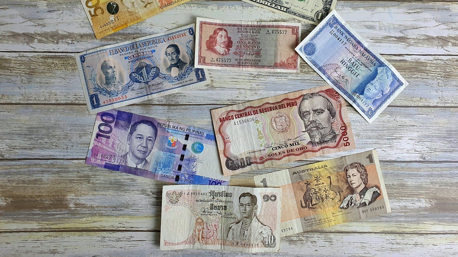 Banknotes from several different currencies spread across a wooden table