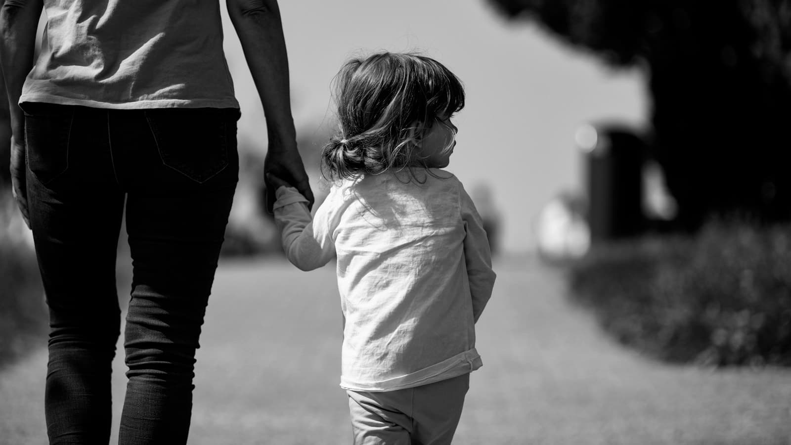 A woman gently holding the hand of a small child as they walk