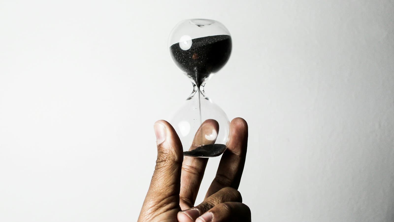 Hand holding a small hourglass with dark sand running through it