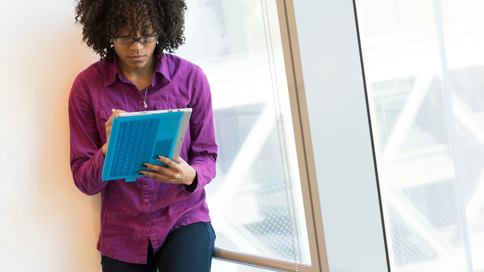 Woman in a purple shirt reviewing documents on a tablet beside a window
