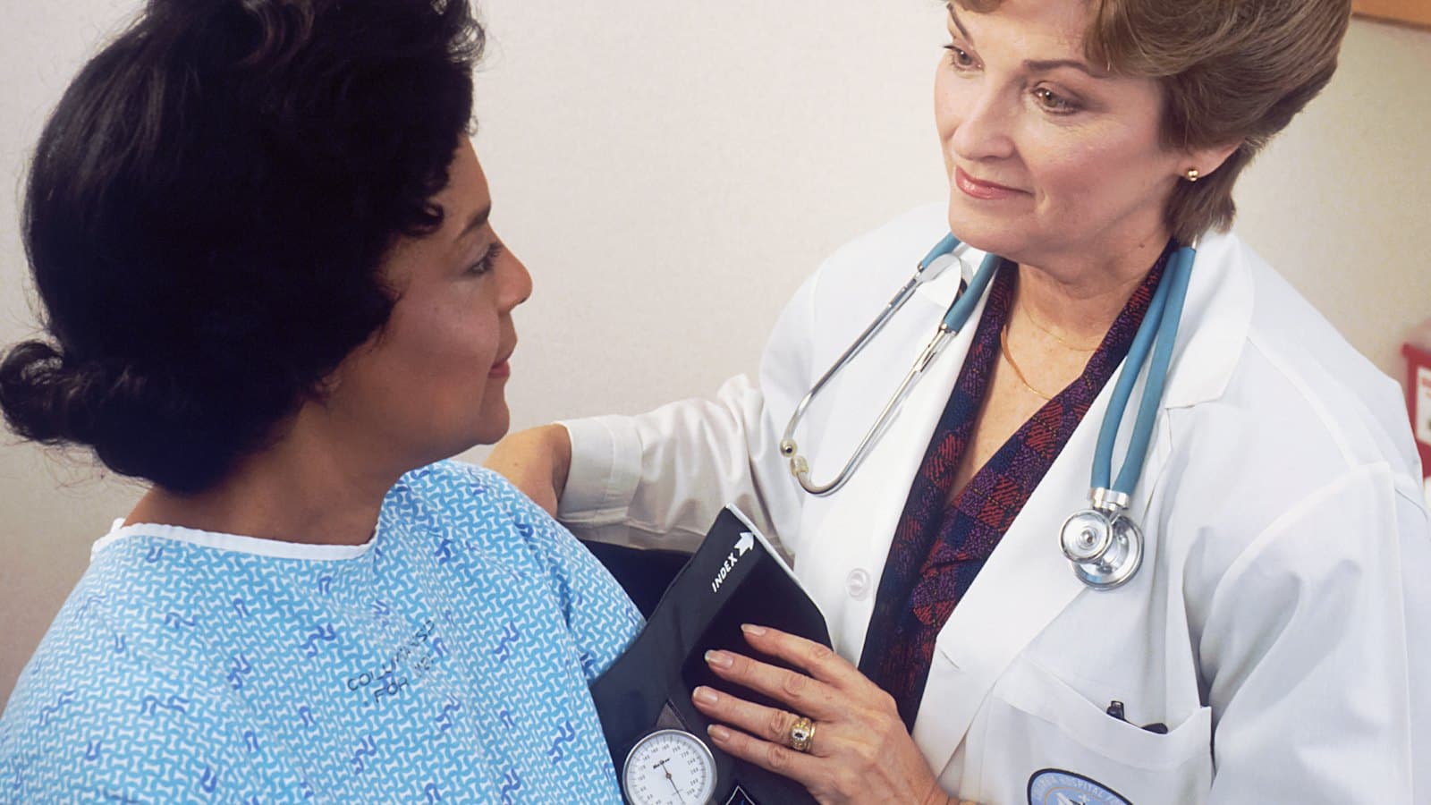 Clinician in a white coat checking a smiling patient's blood pressure