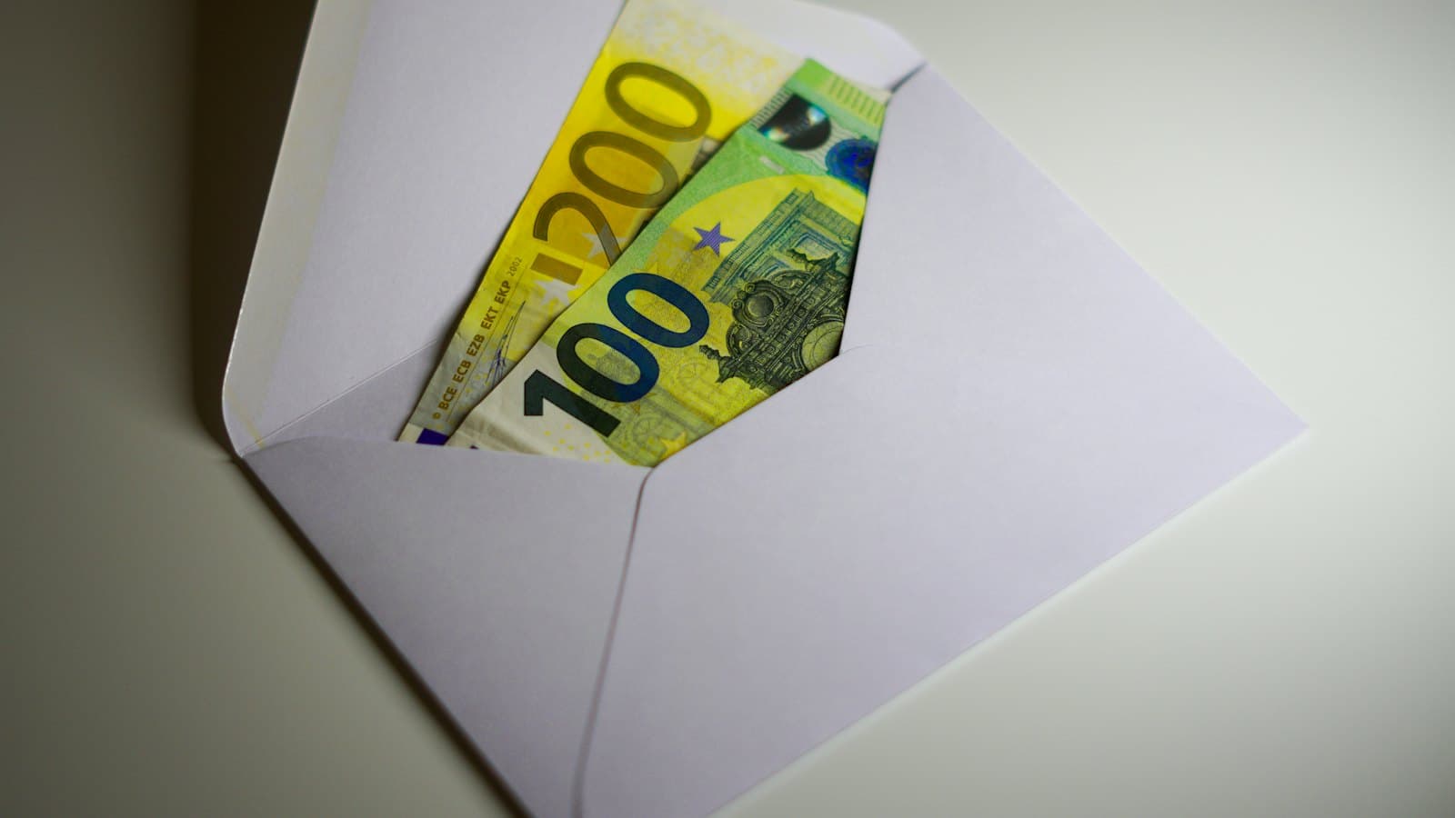 Euro banknotes tucked inside an open white envelope on a table