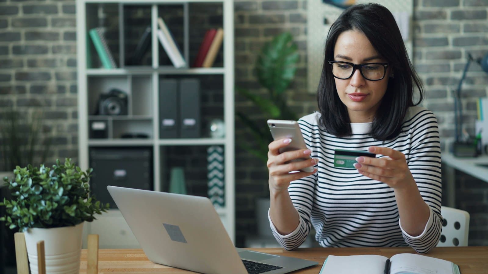 Woman holding a bank card and phone while paying online at her desk