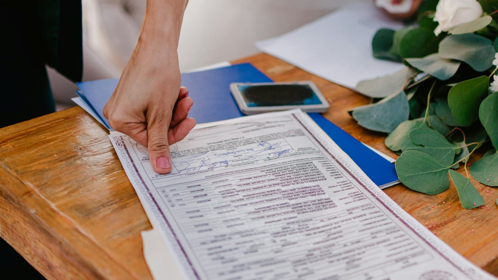 A person pointing at a certificate laid out on a wooden table
