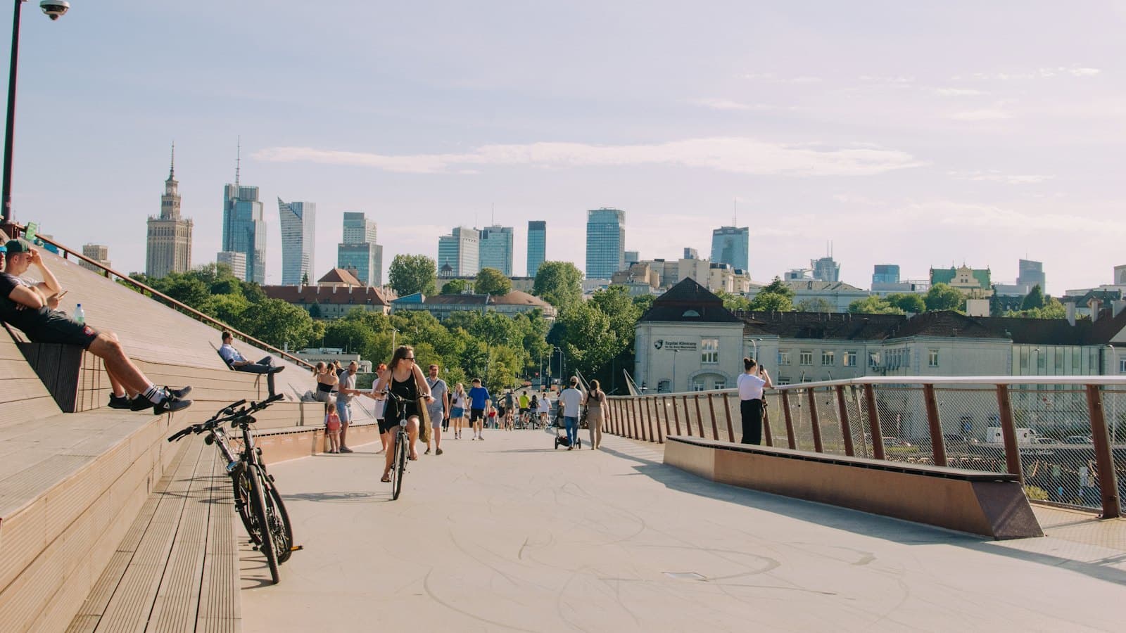 People walking and cycling across a footbridge with the Warsaw skyline in the distance