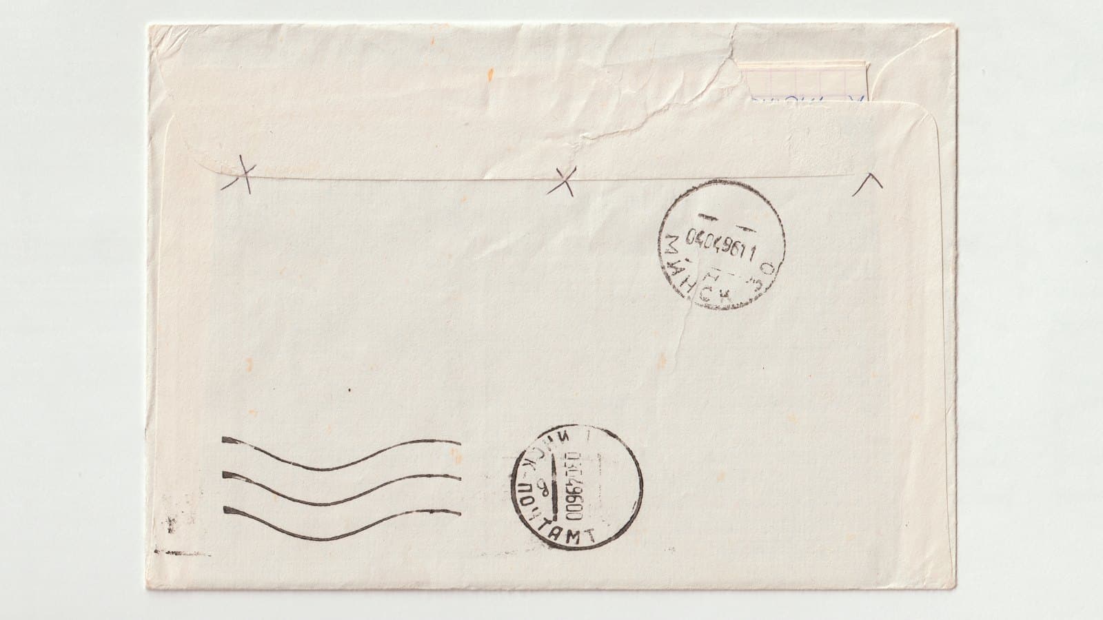 Back of a posted envelope marked with two round foreign postmark stamps