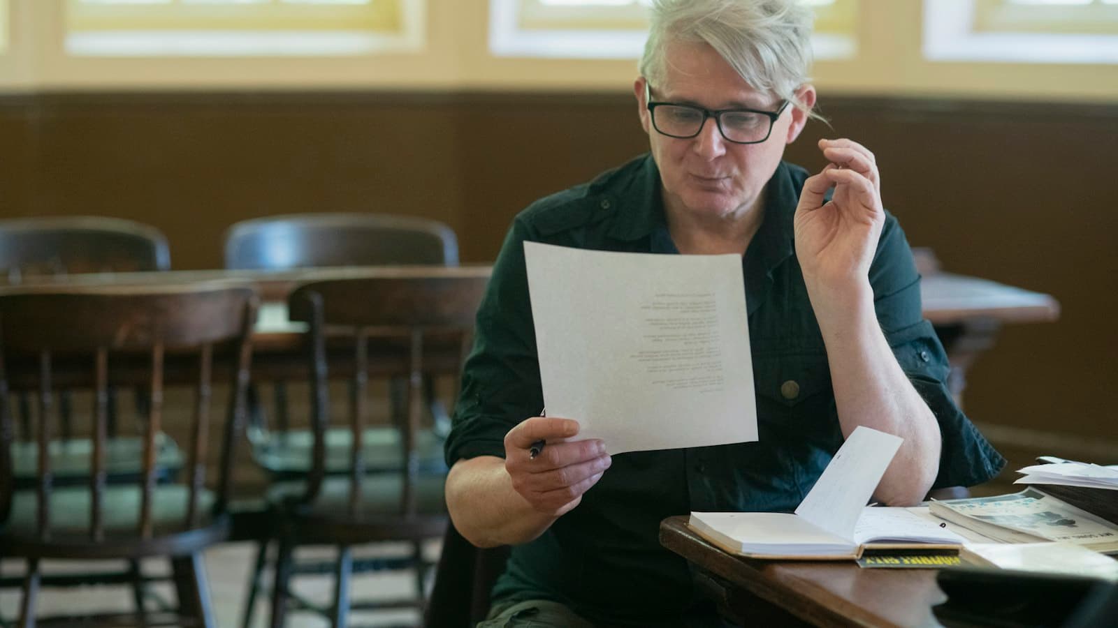 A man sitting at a table carefully reading a sheet of paper