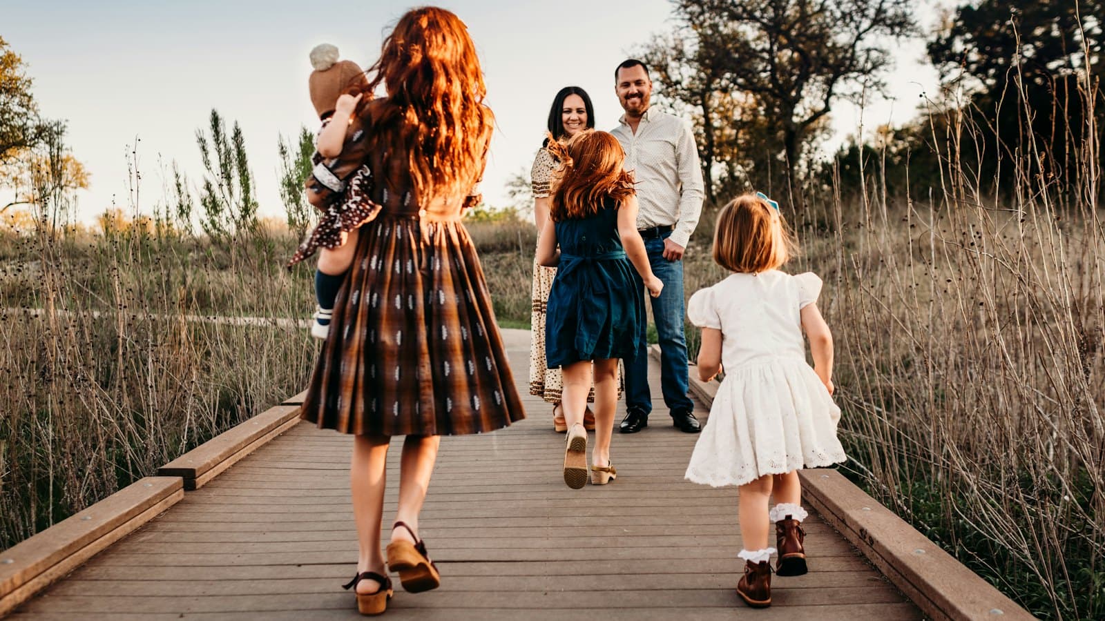 A family walking together along a wooden boardwalk through a field at golden hour