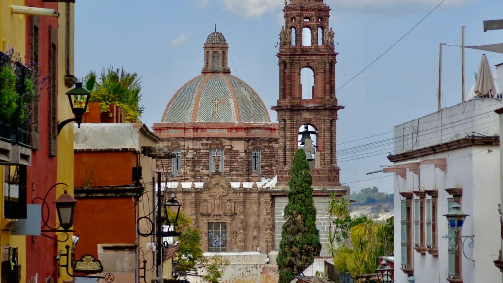 Colorful colonial buildings and lanterns frame a tiled church dome and bell tower in Mexico
