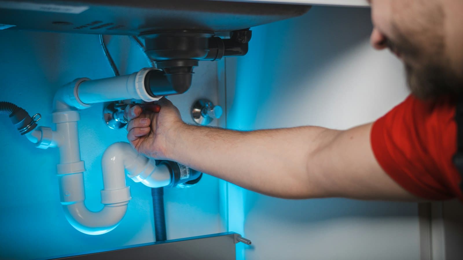 Plumber reaching under a sink to tighten a pipe fitting