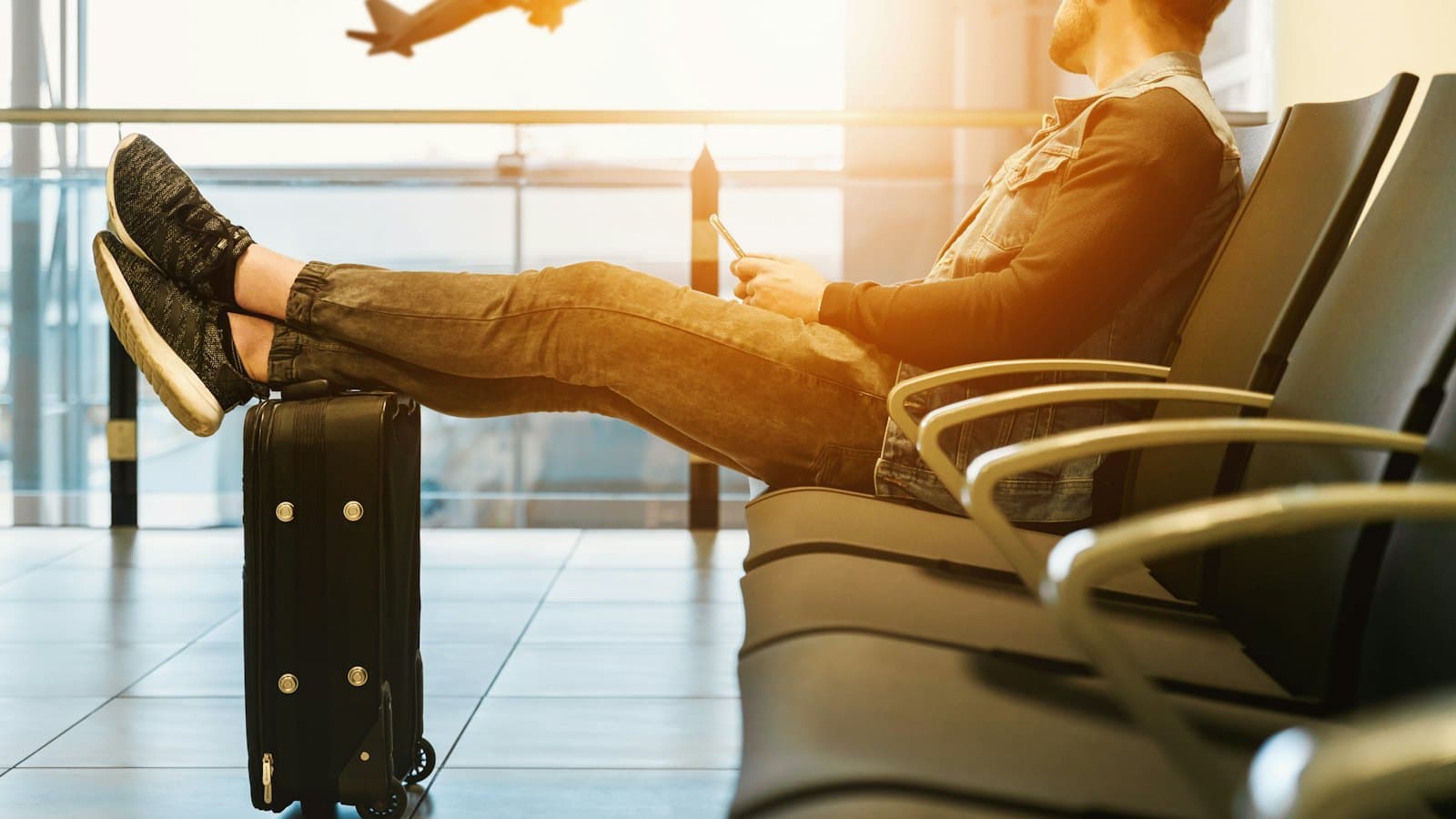 Traveller resting with feet on his luggage, watching a plane from an airport window