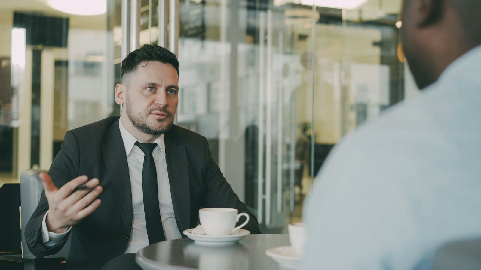 A man in a suit advising a client over coffee at a table